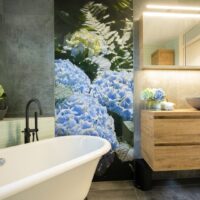 Badkamer met bloemenmuur van blauwe hortensia’s en bijpassende bloemen op houten wastafel